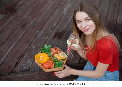 Smiling, Relaxed Blond Woman, Student, Look At Camera, Drink Alcohol And Eating Tasty Food On Plate On Wooden Floor On Patio. Weekend Activity, Picnic On Holiday Celebration And Break In Countryside.