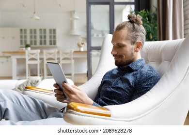 Smiling Relaxed Millennial Gadget User Man Reading Book On Tablet Computer Screen, Watching Movie, Virtual Training Webinar, Using Online App, Browsing Internet, Social Media, Shopping