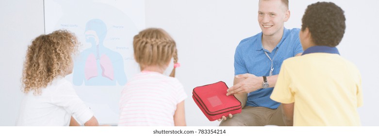 Smiling Rescuer Showing First Aid Kit During Training With Children At School