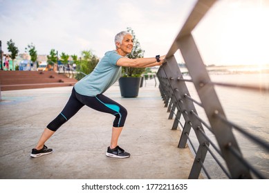 Smiling retired woman stretching legs outdoors. Senior woman enjoying daily routine warming up before running at morning. Sporty lady doing leg stretches before workout  - Powered by Shutterstock