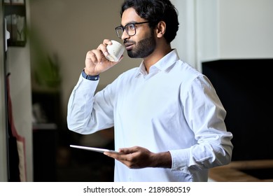 Smiling rich wealthy successful indian business man executive drinking morning coffee enjoying success at work having break starting day in office thinking af daily plans, looking through window. - Powered by Shutterstock