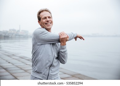Smiling Runner in gray sportswear warming up near the water