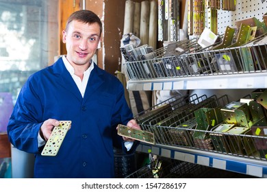 smiling russian man seller wearing uniform having metal furniture in hands in store