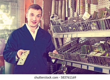 smiling russian man seller wearing uniform having metal furniture in hands in store
