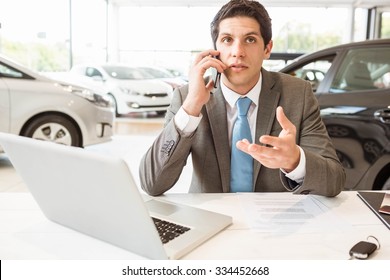 Smiling Salesman Having A Phone Call At New Car Showroom