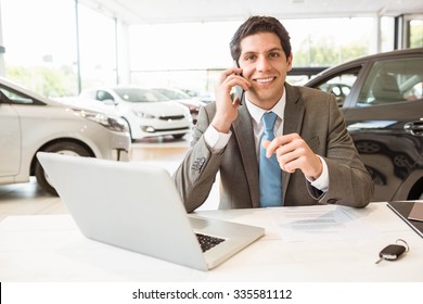 Smiling Salesman Having A Phone Call At New Car Showroom