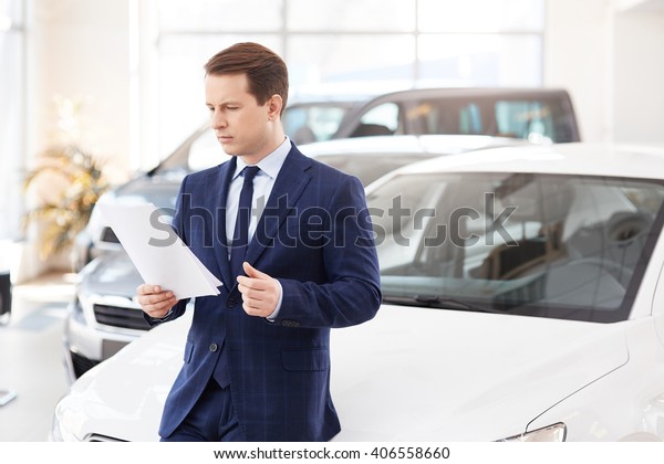 Smiling\
salesman reading a document at new car\
showroom