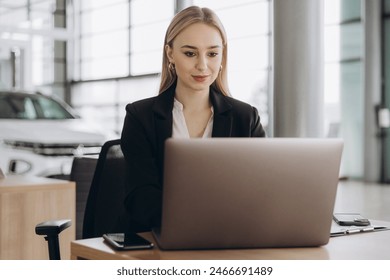 Smiling saleswoman typing on her laptop at new car showroom - Powered by Shutterstock