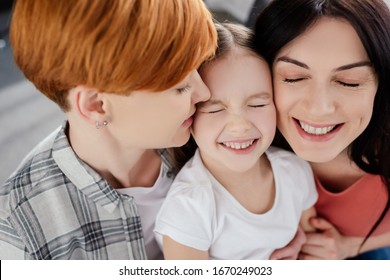 Smiling Same Sex Couple Embracing Kid At Home