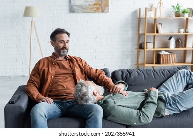 Smiling Same Sex Couple Holding Hands Near Remote Controller On Couch 