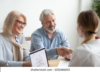Smiling satisfied senior couple making sale purchase deal concluding contract handshaking real estate agent or realtor, happy older family and broker shake hands agreeing to buy new house at meeting