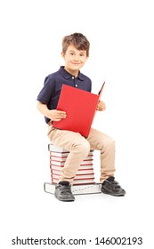 Smiling School Boy Sitting On A Pile Of Books And Reading Isolated On White Background