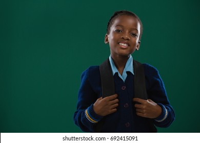 Smiling school girl with backpack standing against chalk board