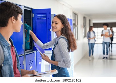 Smiling school girl using locker in campus while talking to friend. Young high school student with guy standing near locker in campus hallway. Friends talking to each other outside the classroom.