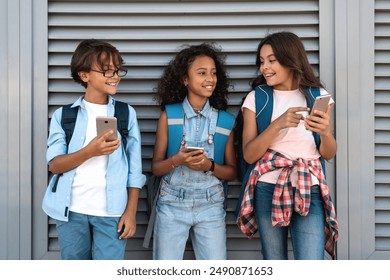 Smiling school kids preteen boy and girls holding smart cell mobile phones gadgets using social media at the street outside during break standing over grey background. - Powered by Shutterstock