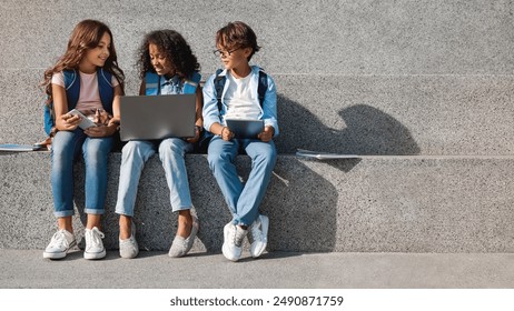 Smiling school kids preteen boys and girls elementary middle pupils children sitting on the stairs and looking in smartphone screen with digital devices laptop tablet in hands outdoors, copy space - Powered by Shutterstock