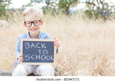 smiling schoolboy in glasses holding blackboard with "back to school" sign ready for school enjoying warm weather in the park - Powered by Shutterstock