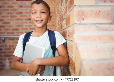 Smiling schoolboy looking at the camera while holding a digital tablet