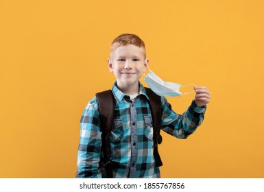 Smiling schoolboy taking off protective face mask over yellow studio background, copy space. Schoolboy holding face mask in hand, using protection against coronavirus while going to school - Powered by Shutterstock