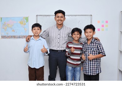 Smiling schoolboy and teacher standing together in front of the classroom, looking at camera and giving thumbs up . Banner for Teacher's Day. - Powered by Shutterstock