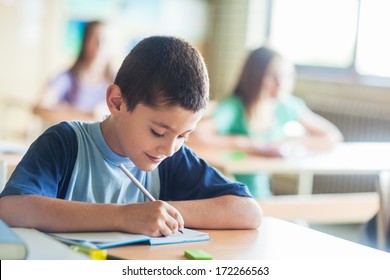 Smiling Schoolboy Writing Notes In Class.