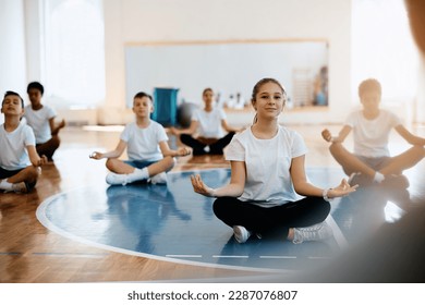 Smiling schoolgirl and her classmates exercising Yoga while having physical education class at school gym. - Powered by Shutterstock