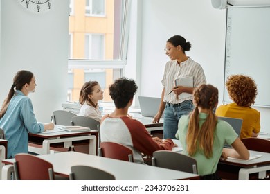 Smiling schoolgirl looking at african american teacher with notebook during lesson in classroom - Powered by Shutterstock