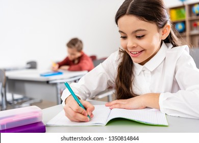 Smiling schoolgirl writing in notebook during lesson in classroom - Powered by Shutterstock