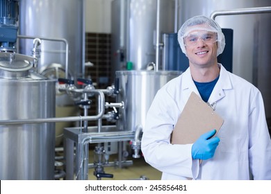 Smiling scientist looking at camera holding a clipboard in the factory - Powered by Shutterstock