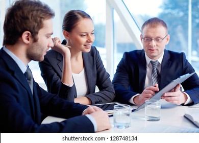 Smiling secretary looking at document held by her boss while listening to his explanation