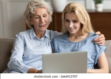 Smiling Senior 60s Mother And Millennial Girl Child Relax At Home Using Modern Laptop Gadget Together, Happy Mature Mom And Adult Daughter Rest On Couch Watch Video Browse Internet On Computer