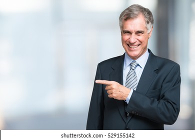 Smiling senior businessman pointing his finger on the white space