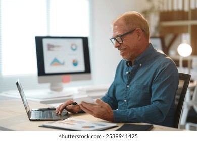 Smiling senior businessman using laptop and smartphone, analyzing financial charts and working with documents at the office - Powered by Shutterstock