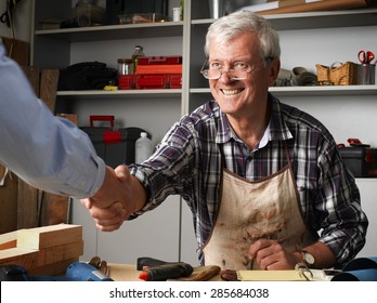 Smiling Senior Carpenter Greeting Customer And Shaking His Hand At Workshop. Small Business.