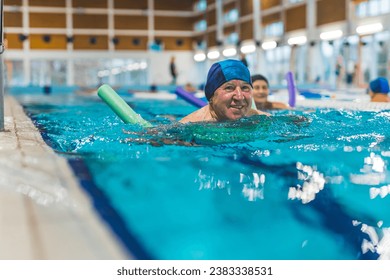 smiling senior Caucasian man with blue swimming cap using a swim noodle in the pool. High quality photo - Powered by Shutterstock