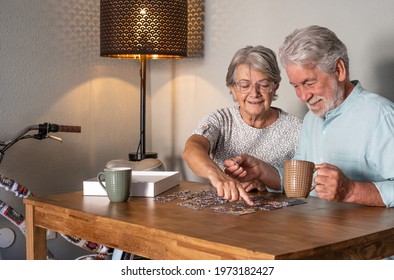Smiling senior couple doing a jigsaw puzzle at home on wooden table. Vintage bicycle in the corner