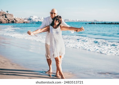 Smiling senior couple enjoying a sunny day at the beach, smiling and embracing each other while dressed in light summer clothes, conveying love, happiness, and companionship - Powered by Shutterstock