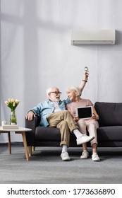 Smiling senior couple holding digital tablet and remote controller of air conditioner at home