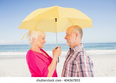 Smiling senior couple holding umbrella on the beach - Powered by Shutterstock