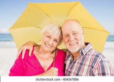 Smiling senior couple holding umbrella on the beach - Powered by Shutterstock