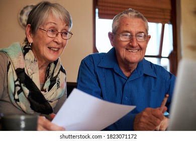 Smiling Senior Couple At Home Checking Personal Finances On Laptop