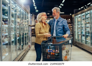 Smiling senior couple looking at each other, enjoying shopping in nearby grocery store, pushing shopping trolley - Powered by Shutterstock