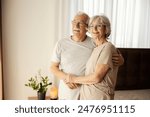 Smiling senior couple in love hugging at nursing home and looking through window.