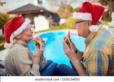 Smiling Senior Couple On Christmas In Santa Hats Eating Watermelon