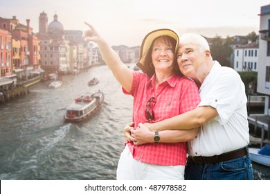 Smiling Senior Couple Pointing Finger In Front Of Grand Canal In Venice