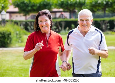 Smiling Senior Couple Running Together In Park