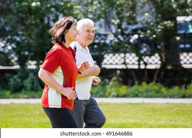 Smiling Senior Couple Running Together In Park