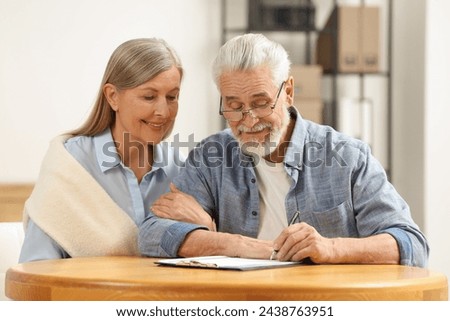 Smiling senior couple signing Last Will and Testament indoors