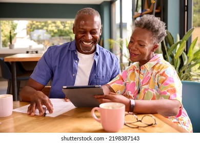 Smiling Senior Couple Sitting Around Table At Home Reviewing Finances Using Digital Tablet - Powered by Shutterstock