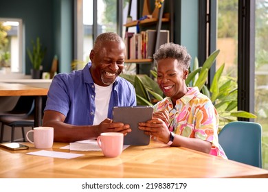 Smiling Senior Couple Sitting Around Table At Home Reviewing Finances Using Digital Tablet - Powered by Shutterstock